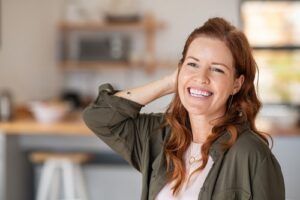 Model smiling and holding her hair with her hand. She is in a brightly lit kitchen.